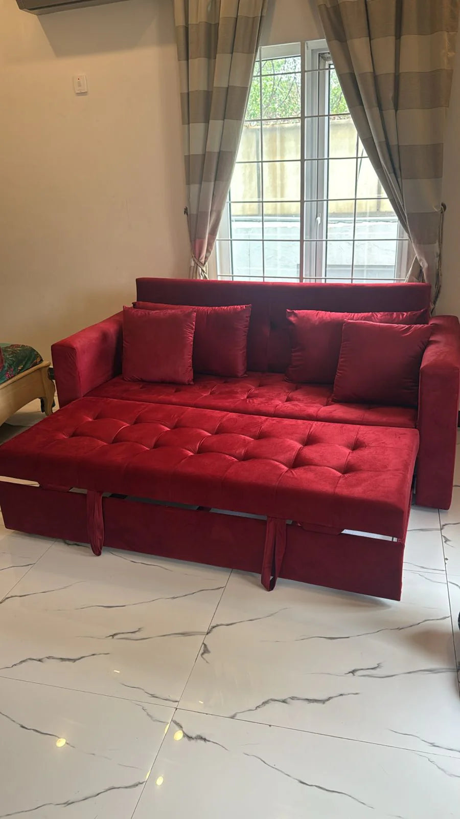Red sofa bed in a customer's room with a window and curtains.